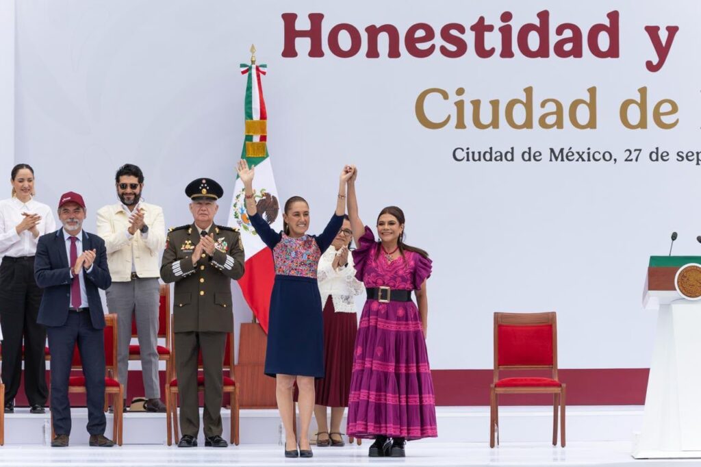 Claudia Sheinbaum y Clara Brugada levantan las manos unidas en el templete del Zócalo, acompañadas de autoridades.